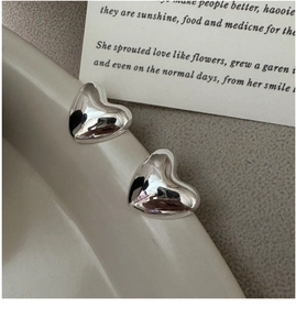 Close-up of polished S925 sterling silver heart studs on a ceramic tray rim