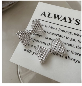 Macro detail of S925 sterling silver bow earrings featuring a textured granulated finish