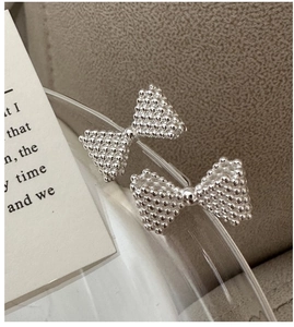 Macro view of silver bow earrings with textured caviar finish on a glass rim