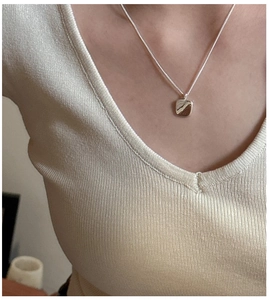 Macro shot of minimalist square silver pendant necklace worn with beige knitwear