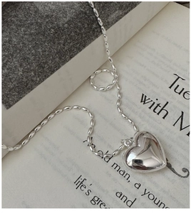 Macro detail of a polished silver heart pendant on a unique beaded chain necklace