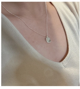 Close-up of a square minimalist silver pendant necklace on a beige knit sweater