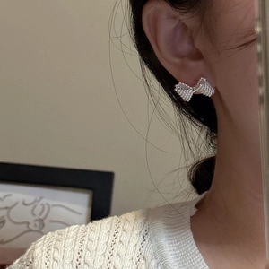 S925 sterling silver bow earrings with woven texture worn by a model on a beige sweater