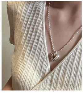 Close-up of a silver hollow heart pendant necklace worn on a beige striped sweater
