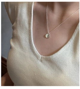Close-up of a minimalist S925 sterling silver round pendant necklace on beige knitwear