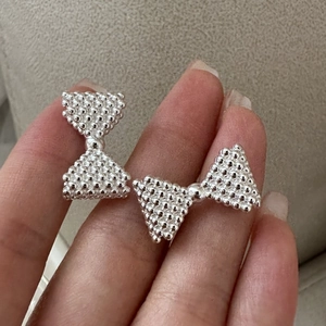 Handheld view of S925 sterling silver bow earrings with textured metal bead details