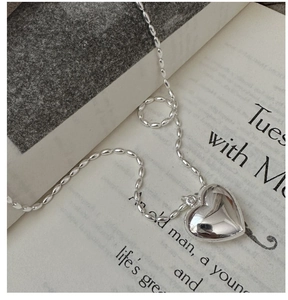 Macro detail of silver rice bead chain and polished heart pendant on a book page