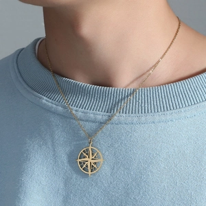 Close-up of golden compass pendant necklace with starburst design on a knitted top