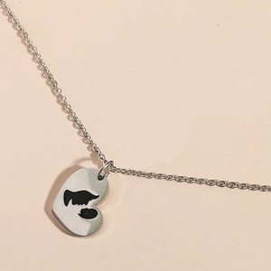 Collier cœur argenté avec silhouette noire mère-enfant sur fond rose clair élégant