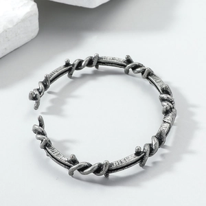 Macro detail of silver gray braided barbed wire open bracelet in punk vintage metal style