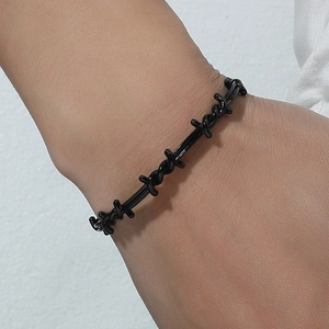 Close-up of a black punk-style barbed wire bracelet worn by a model in a minimalist setting