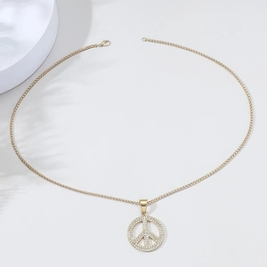 Close-up of golden peace sign pendant with pavé crystals on a minimalist chain