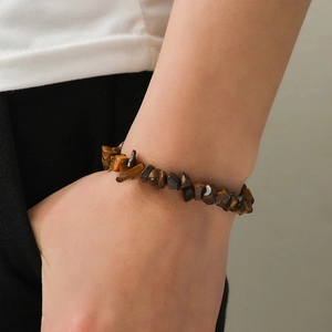 Detail of natural tiger eye stone chip bracelet worn on wrist with golden silk texture