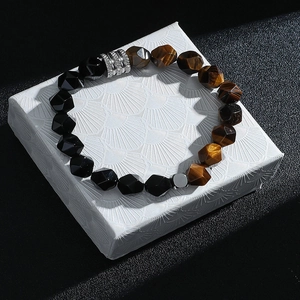 Détail d'un bracelet en œil de tigre facetté et perles noires sur un coffret cadeau blanc