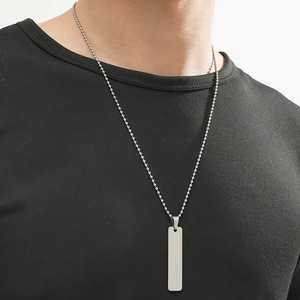 Gros plan d'un pendentif barre minimaliste en acier inoxydable argenté sur chaîne à billes
