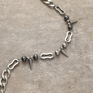 Collier punk gothique avec chaîne cubaine argentée, rivets et perles sur fond pierre