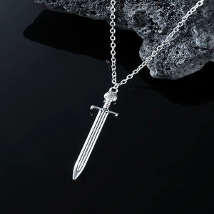 Macro shot of silver metal sword pendant with detailed hilt on dark volcanic rock