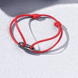 Bracelet tressé rouge créant une ombre en forme de cœur sur une surface en pierre grise