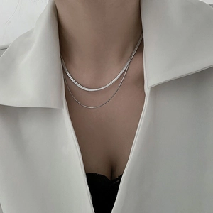 Dettaglio della collana a doppio strato in maglia serpente argento su giacca bianca