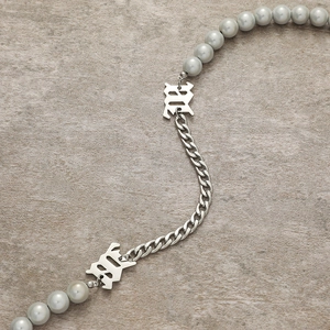 Collier lettre M gothique avec perles grises et chaîne cubaine argentée sur pierre