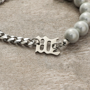 Gothic style Cuban chain bracelet with letter M pendant and grey pearls on stone surface