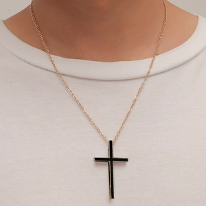 Minimalist black cross pendant on gold chain necklace worn over a white T-shirt