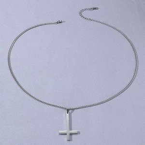 Détail macro du pendentif croix inversée argentée avec chaîne à fermoir mousqueton