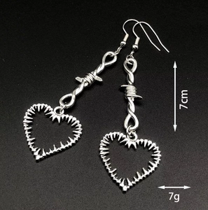Détail de boucles d'oreilles cœur épine argentées au style punk et design barbelé