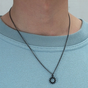 Close-up of minimalist black gear sun pendant necklace worn on a model's neck