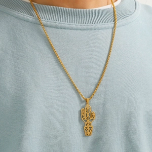 Detail of a gold geometric cactus pendant on a box chain worn over a light blue sweatshirt