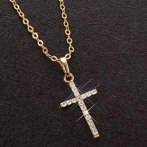 Classic gold cross pendant necklace with sparkling clear crystals on black texture background