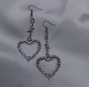 Détail de boucles d'oreilles cœur barbelé en argent sur tissu velours gris