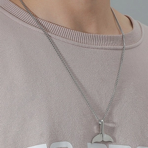 Minimalist silver whale tail pendant necklace for women on a waffle knit shirt background