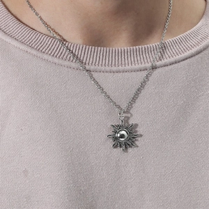 Close-up of a vintage silver sun pendant necklace worn on a ribbed crew neck shirt