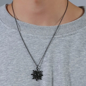 Detail of sunburst pendant with black gemstone on a metallic necklace worn on grey knitwear