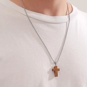 Close-up of a vintage wood cross pendant on a silver rope chain worn on a white t-shirt
