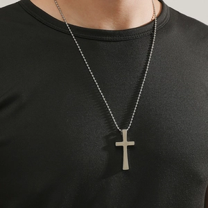 Gros plan d'un pendentif croix argenté avec chaîne à billes porté par un mannequin homme