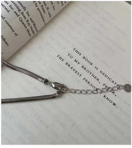 Macro detail of S925 sterling silver flat snake chain with lobster clasp on a book