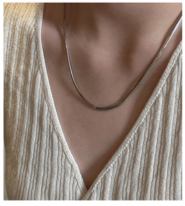 Close-up of minimalist gold-tone snake chain necklace on model neck with knit background