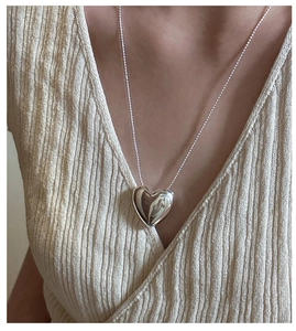 Close-up of a polished silver heart pendant on a bead chain necklace worn by a model