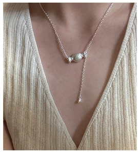 Dettaglio ravvicinato di una collana in argento con ciondolo a caramella e catena a strati