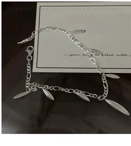 Detailed close-up of matte silver bamboo leaf pendants on a Figaro chain bracelet