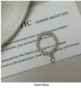Detail shot of a silver beaded ring with heart charm on minimalist white card art