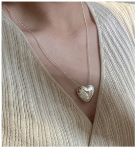 Close-up of polished silver heart pendant on a thin chain over beige knitwear