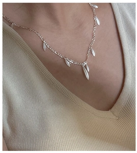 Detail of silver S925 necklace with leaf charms on Figaro chain worn on model neck