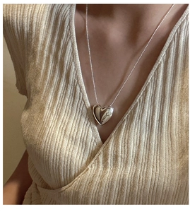 Polished silver heart pendant necklace on beige ribbed knit sweater close-up view