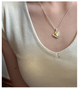 Detail of mixed-metal heart pendant on a thin silver chain worn by a model
