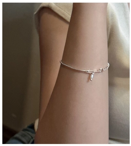 Detail of a dainty S925 sterling silver snake chain bracelet with a pearl pendant on a wrist