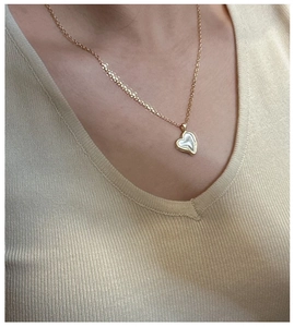 Detail view of heart-shaped shell necklace pendant with gold trim on knit sweater
