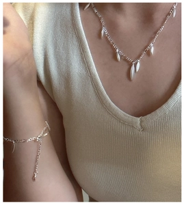 Detail of silver S925 drop charm necklace and bracelet set on a knit top